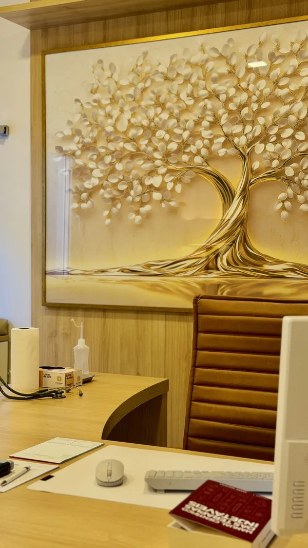 Detalhe da mesa da médica com estetoscópio e o quadro da árvore dourada no consultório da Dra. Franciele
